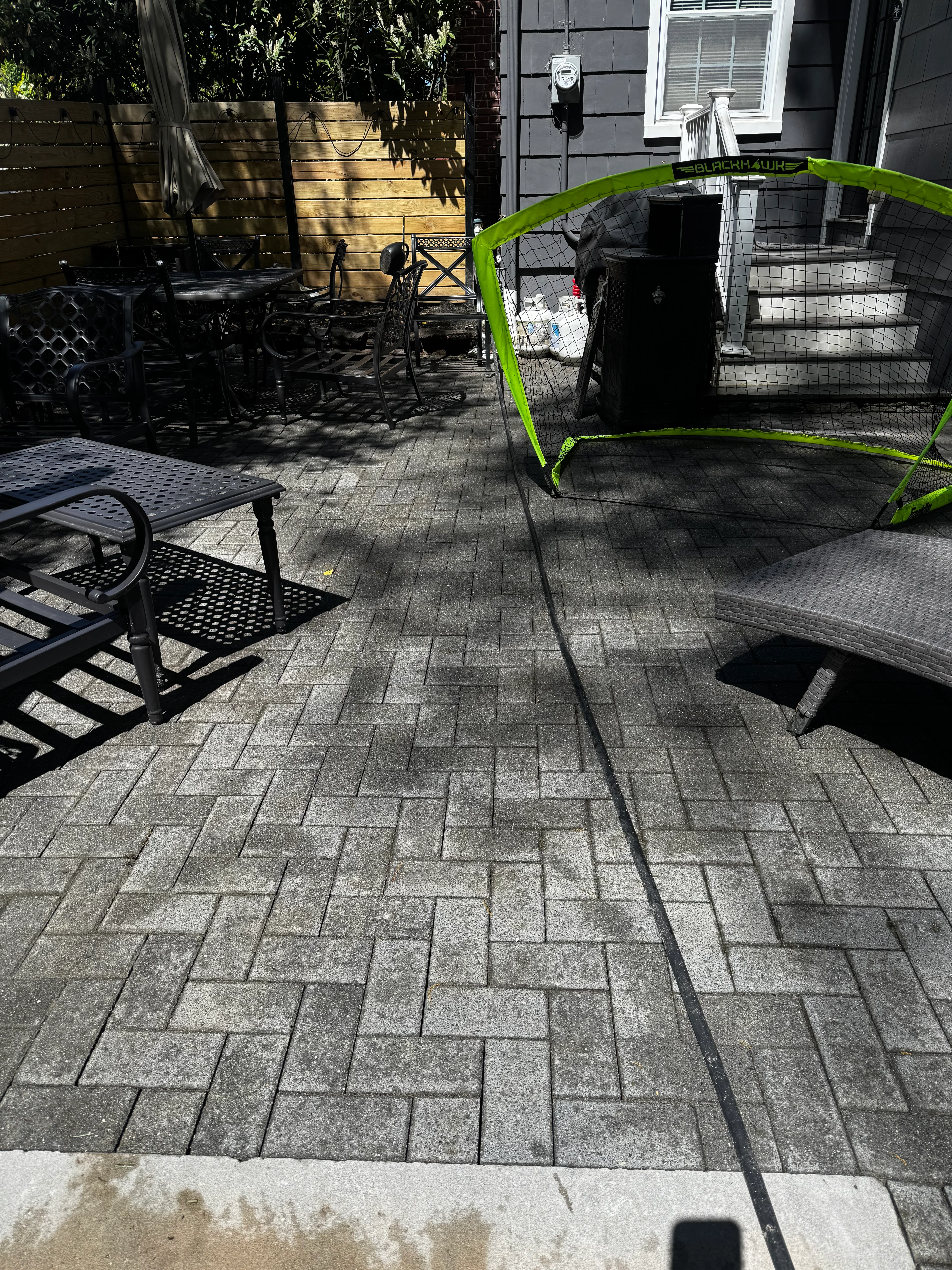 Cleaned herringbone concrete paver patio with pressure washing equipment and green soccer goal